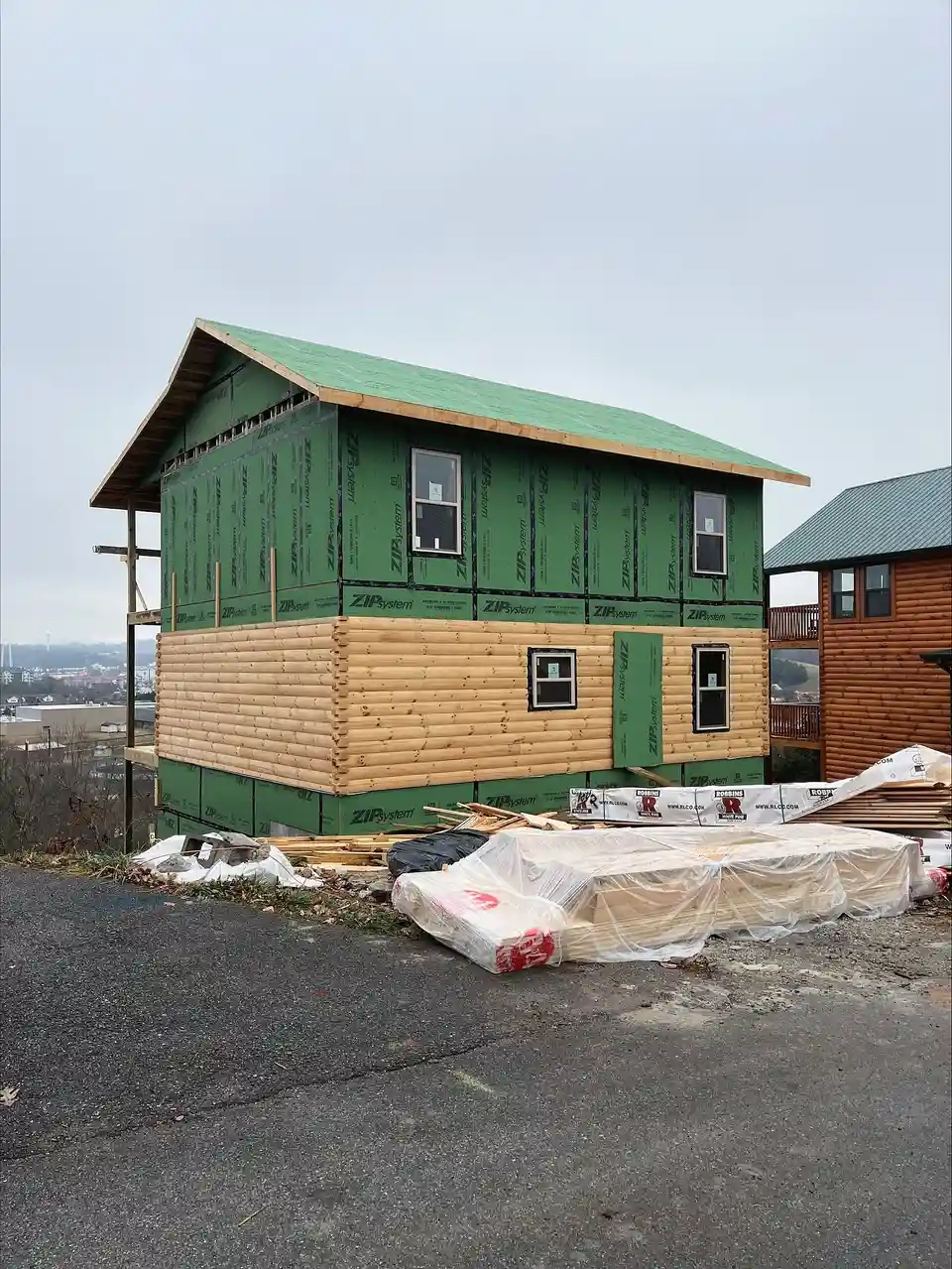 Cost Savings Consulting: cabin with wall sheathing and log siding going on, wrapped material staged in front